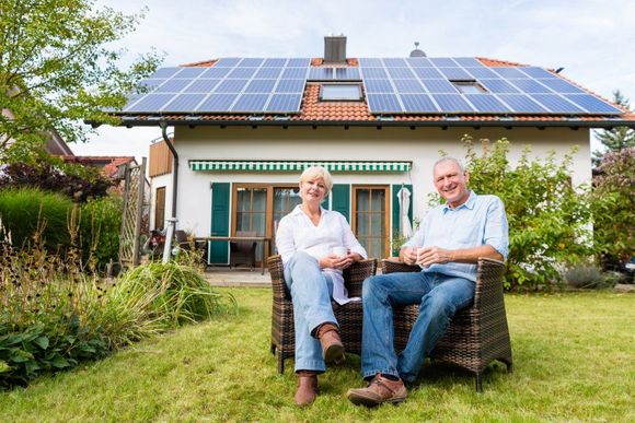 Mann und Frau im Garten ihres von Solarpaneelen bedeckten Hauses